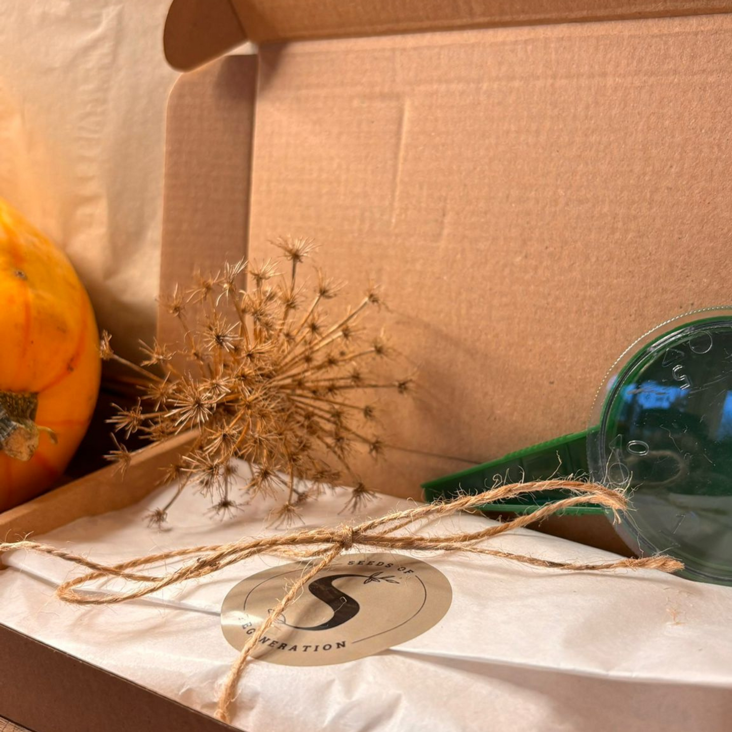 Een verpakte bruine cadeaubox met sticker naast een witte zaaddispenser op een natuurlijke achtergrond