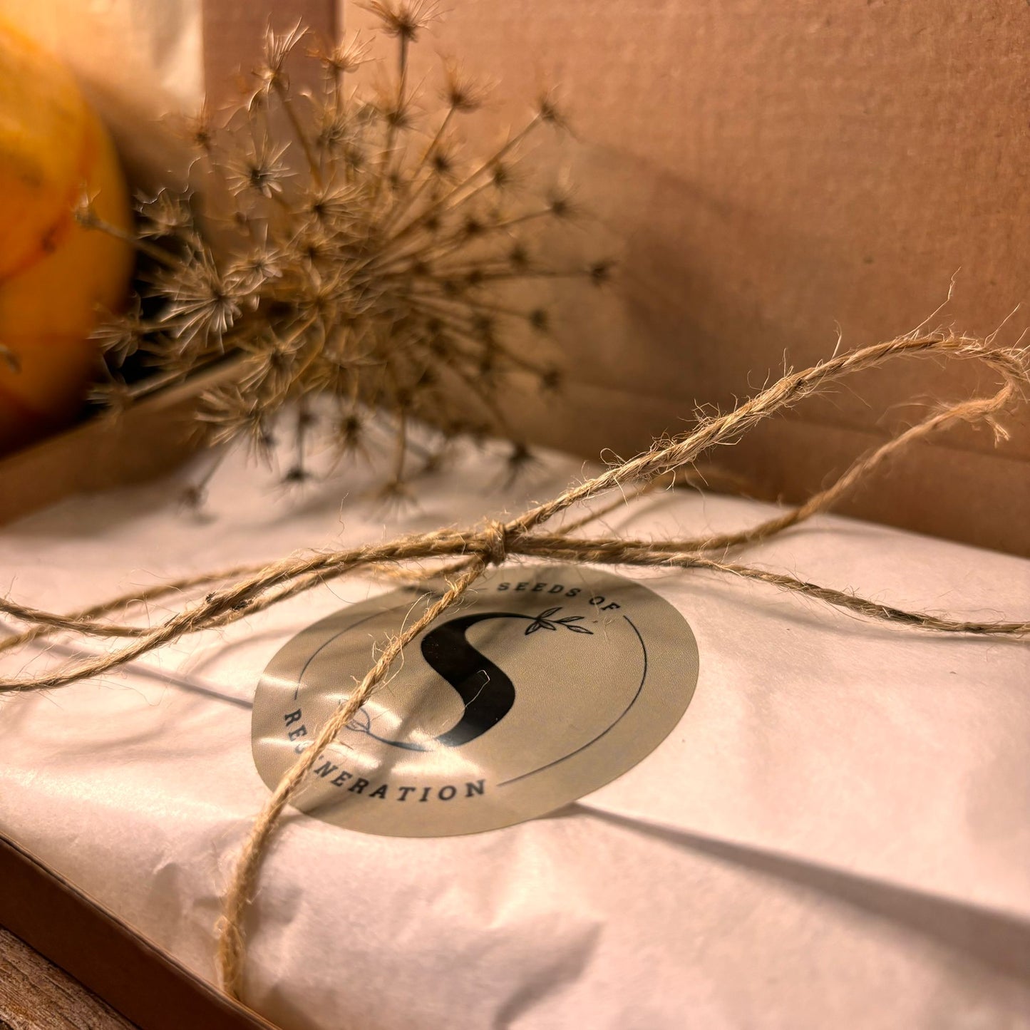 Een elegant verpakte bruine cadeaubox met decoratieve sticker en geschenkkaart op een natuurlijke achtergrond