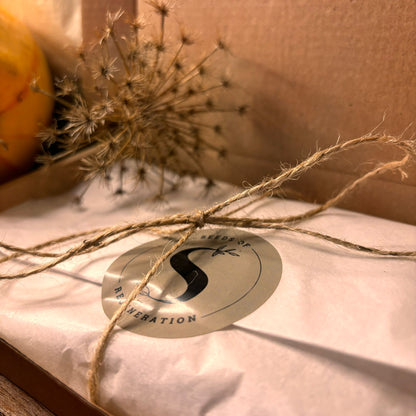 Een elegant verpakte bruine cadeaubox met decoratieve sticker en geschenkkaart op een natuurlijke achtergrond